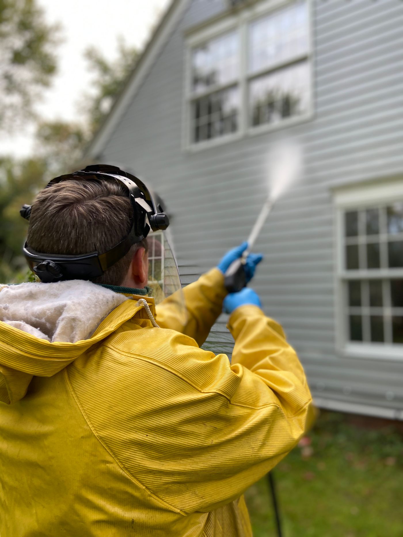 A person cleaning residential siding with a pressure washer